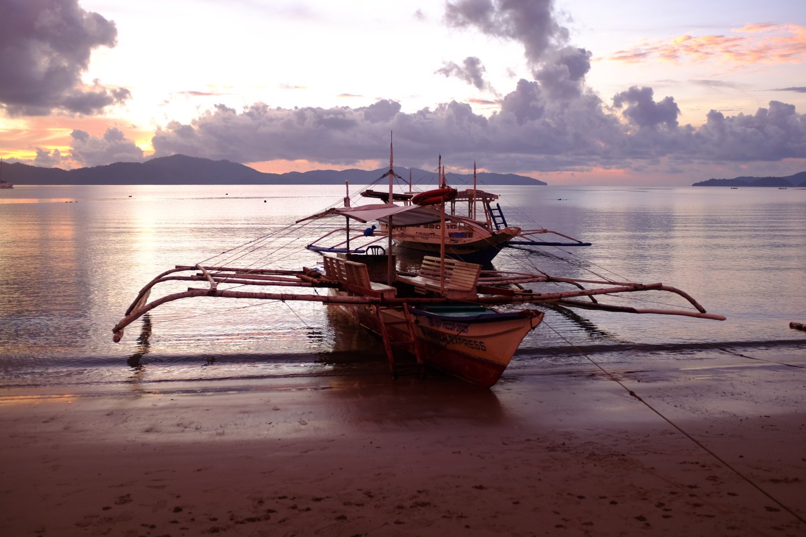 Boats are anchored on the beach at Port Barton, Philippines while the sun sets.