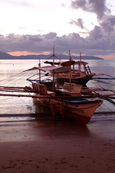 Boats are anchored on the beach at Port Barton, Philippines while the sun sets.