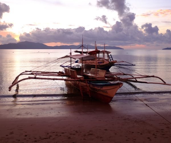 Boats are anchored on the beach at Port Barton, Philippines while the sun sets.