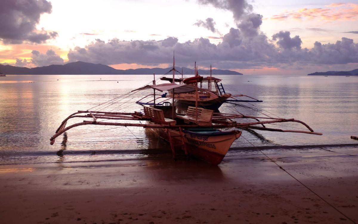 Boats are anchored on the beach at Port Barton, Philippines while the sun sets.