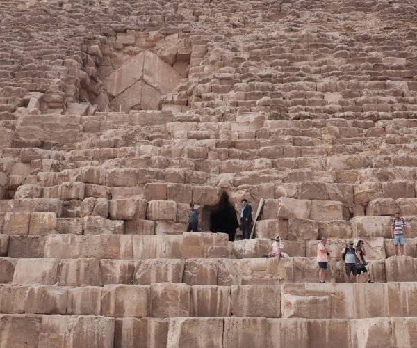 A group of people standing over the massive stones near the entrance of the Great Pyramid.